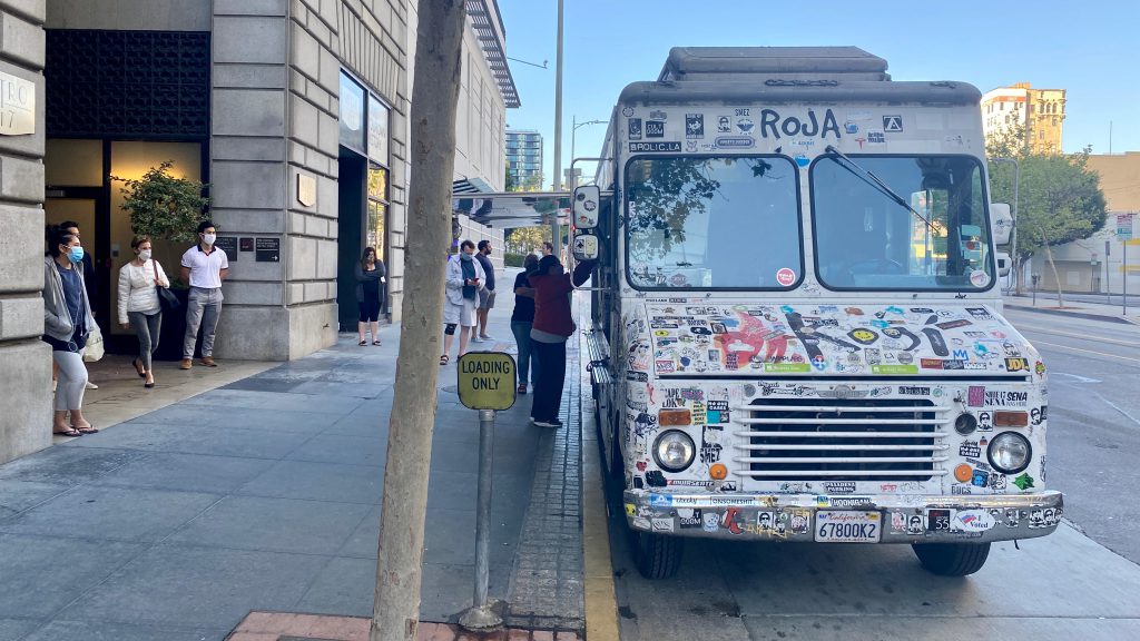 LOS ANGELES, CA, APR 2020: masked residents in Downtown wait for food at sticker-covered Kogi catering truck, parking outside apartments during Covid-19 virus lock down.